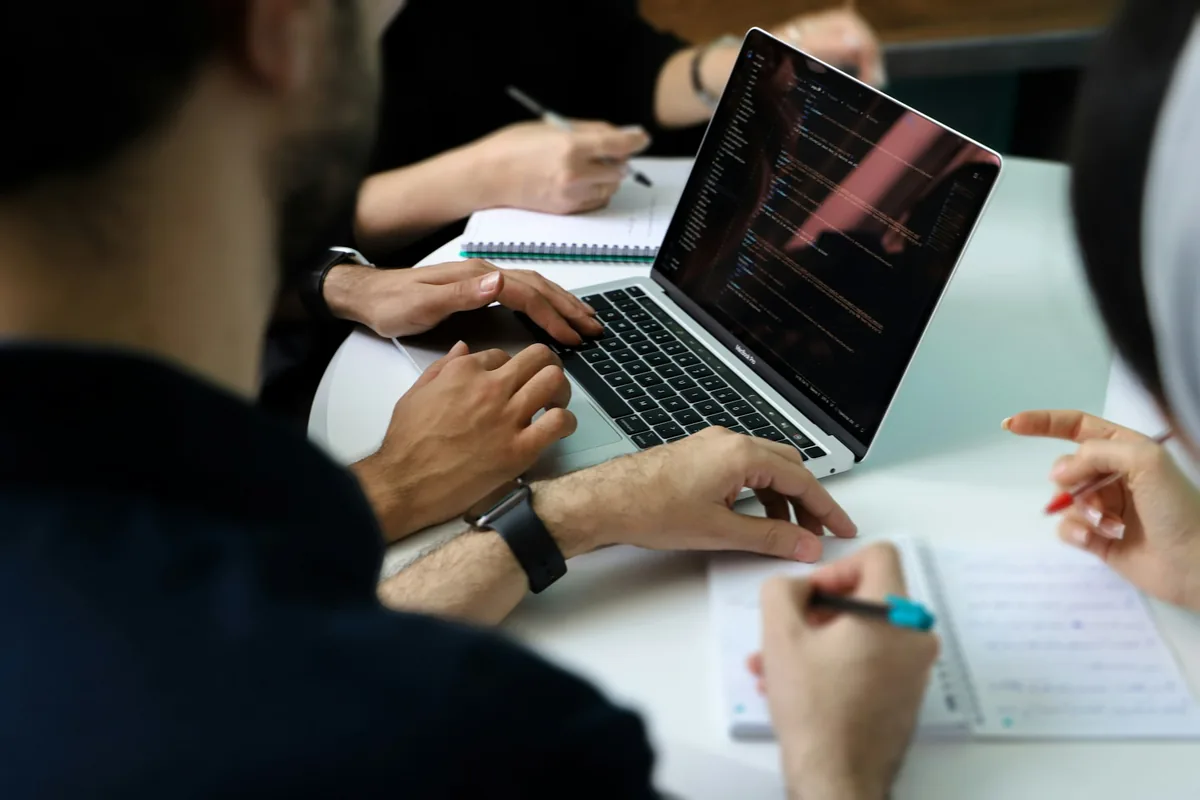 Varias personas reunidas alrededor de un portátil en una mesa de trabajo